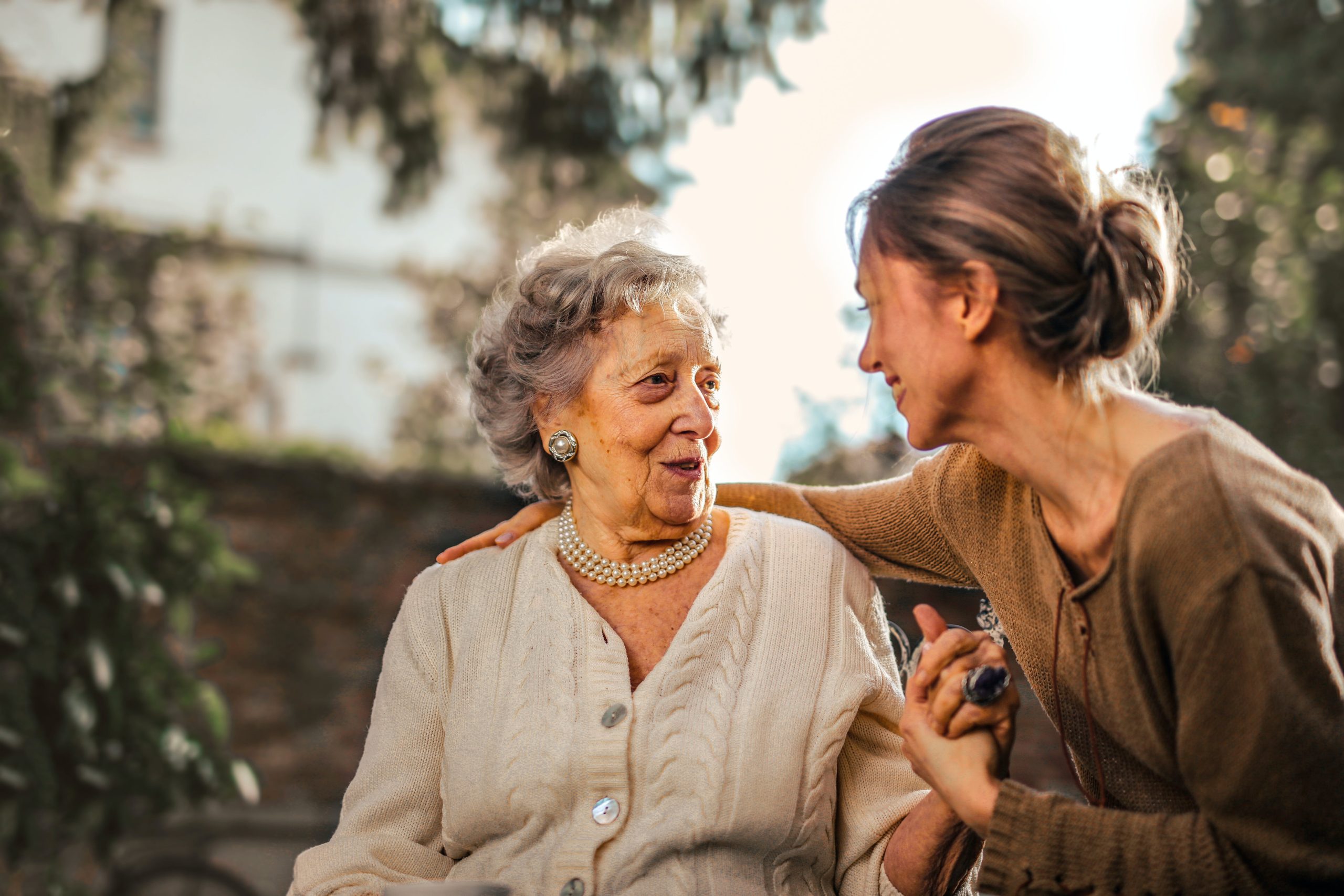 Una persona adulta tiene la mano sulla spalla a una signora anziana, si guardano sorridendo.